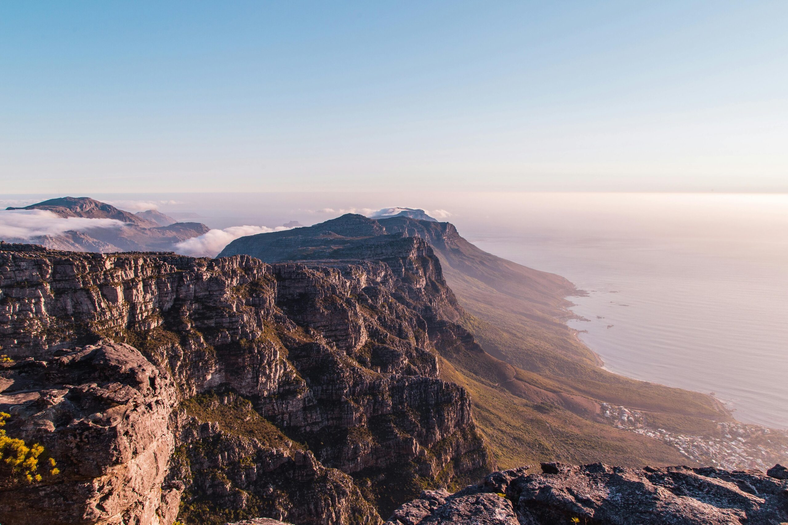 A panoramic view of rocky cliffs and mountains overlooking the ocean at sunrise, with soft clouds rolling over the landscape—just one of our latest specials for nature lovers seeking breathtaking scenery.